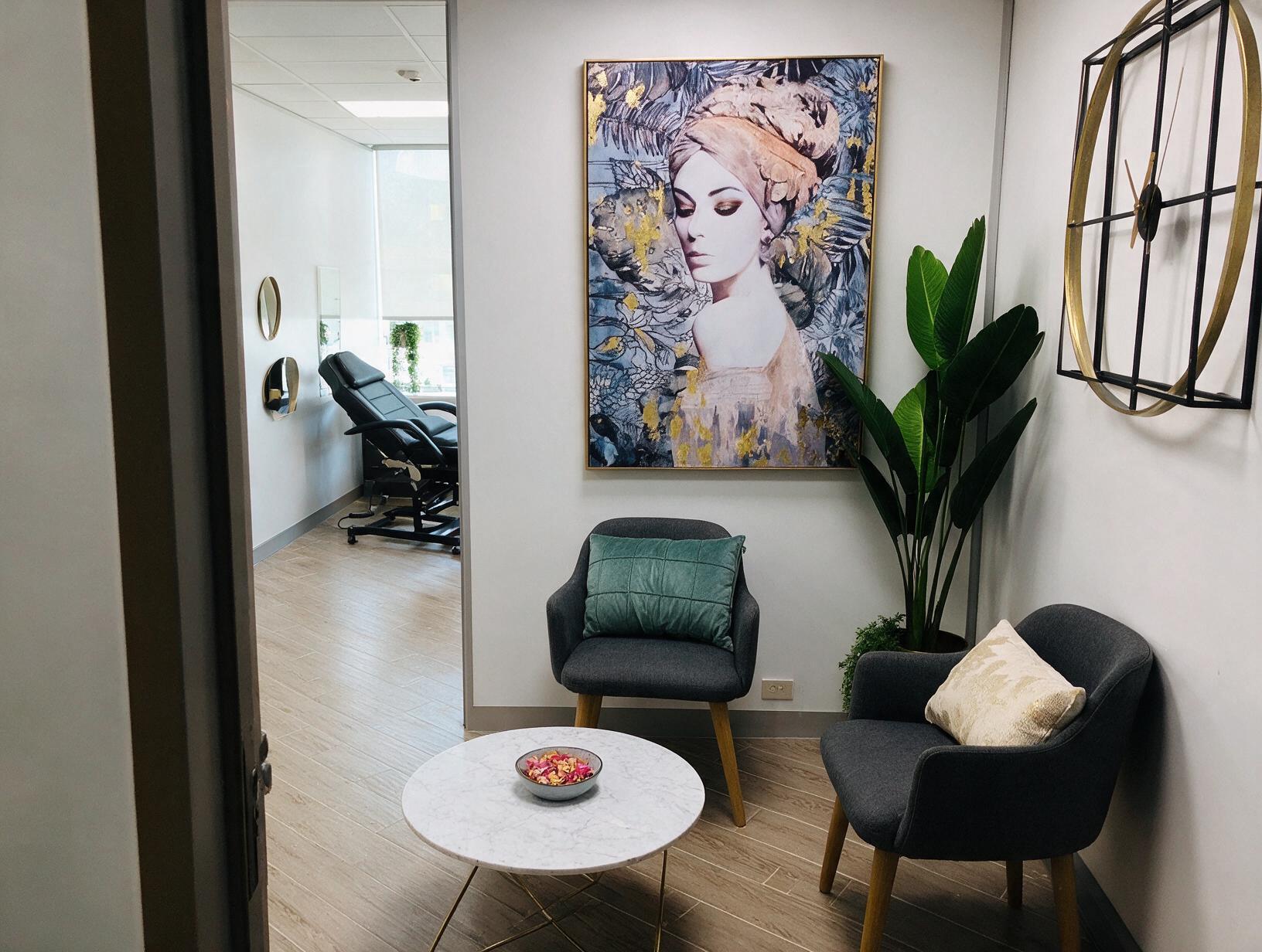 Waiting nook with two grey armchairs, marble coffee table, large framed portrait and plant